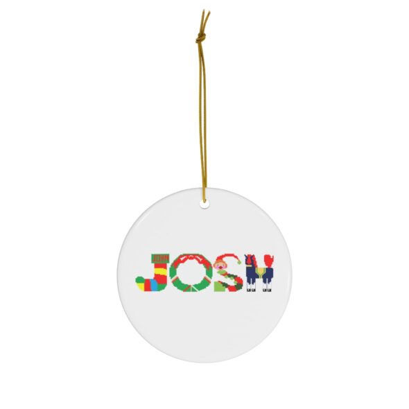 White ceramic ornament with text ‘Josh’ in colourful Christmas themed lettering, with gold hanging loop