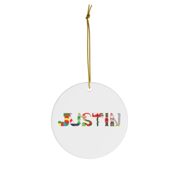 White ceramic ornament with text ‘Justin’ in colourful Christmas themed lettering, with gold hanging loop