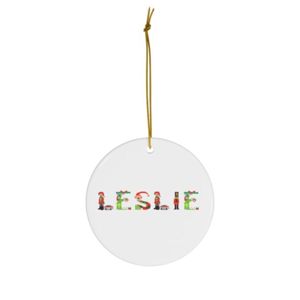 White ceramic ornament with text ‘Leslie’ in colourful Christmas themed lettering, with gold hanging loop
